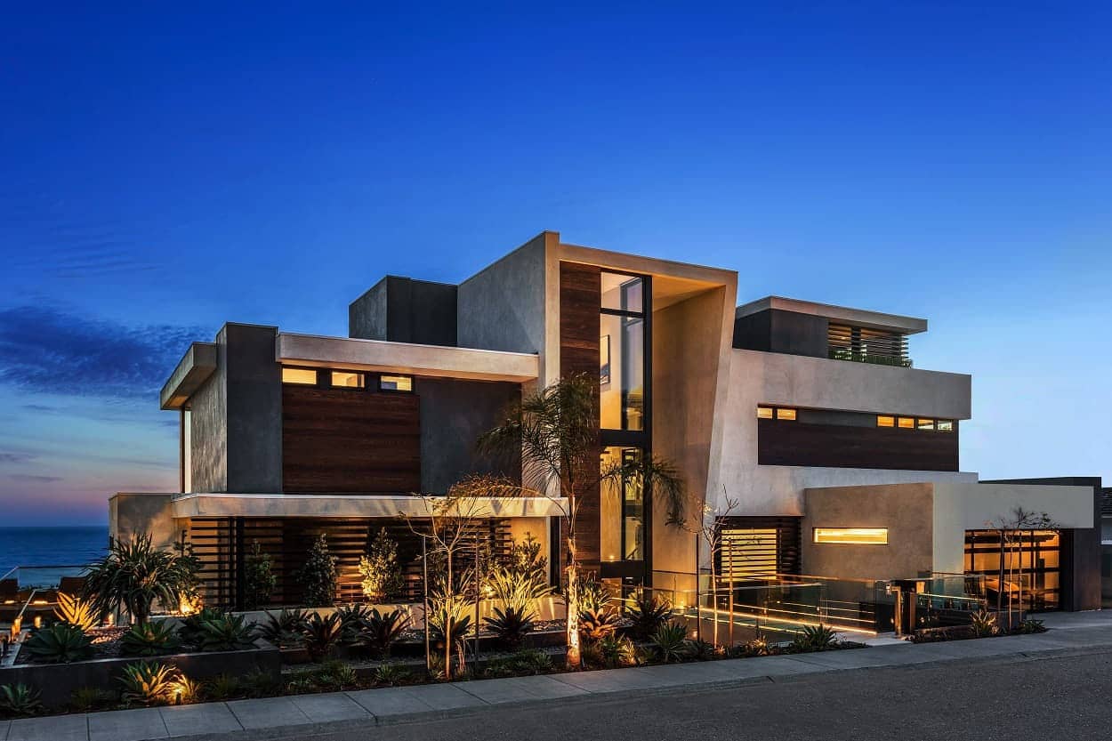 A modern coastal home lit from within at dusk